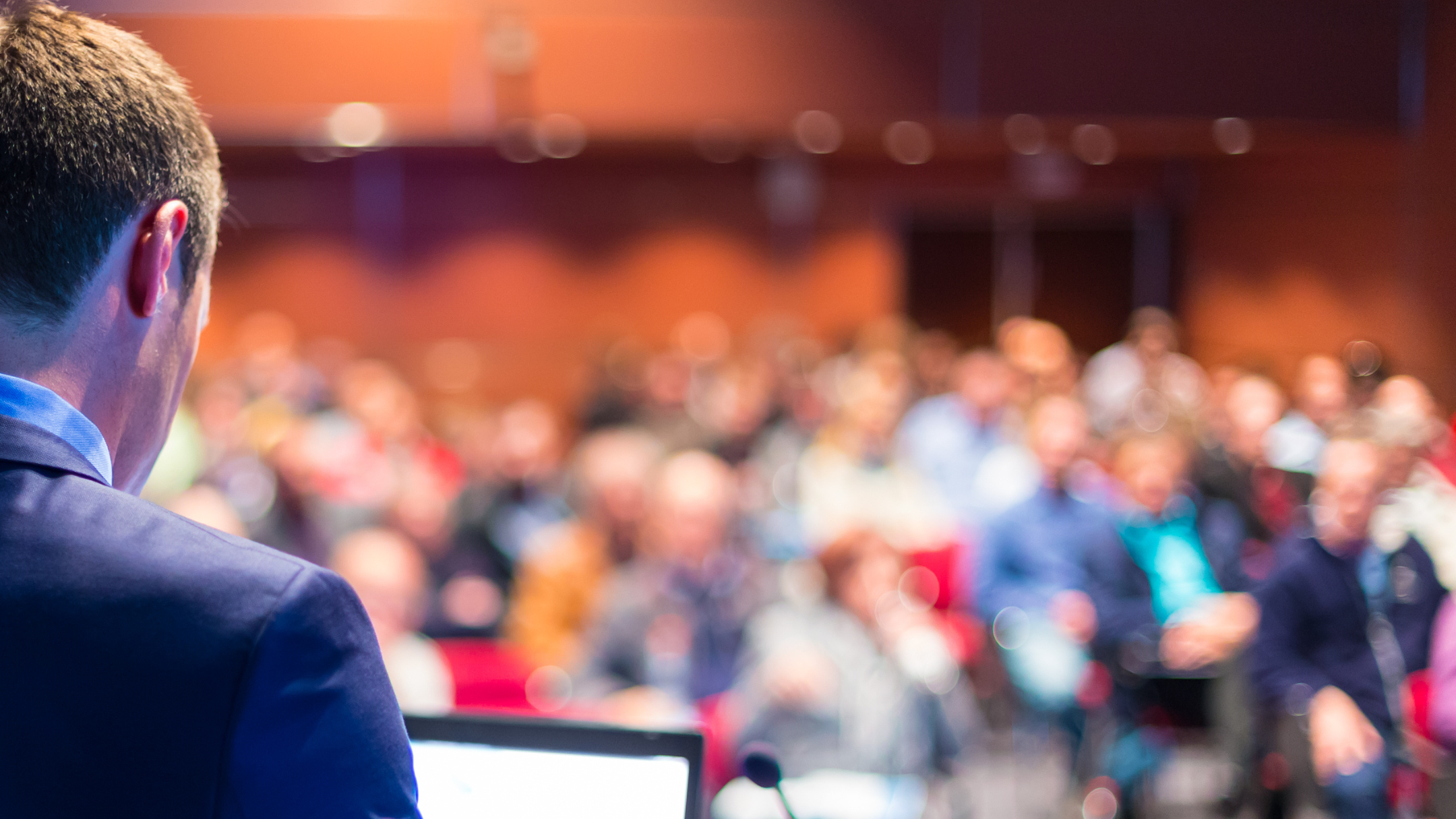 Sala konferencyjna pełna słuchaczy. Na pierwszym planie znajduje się prelegent.
