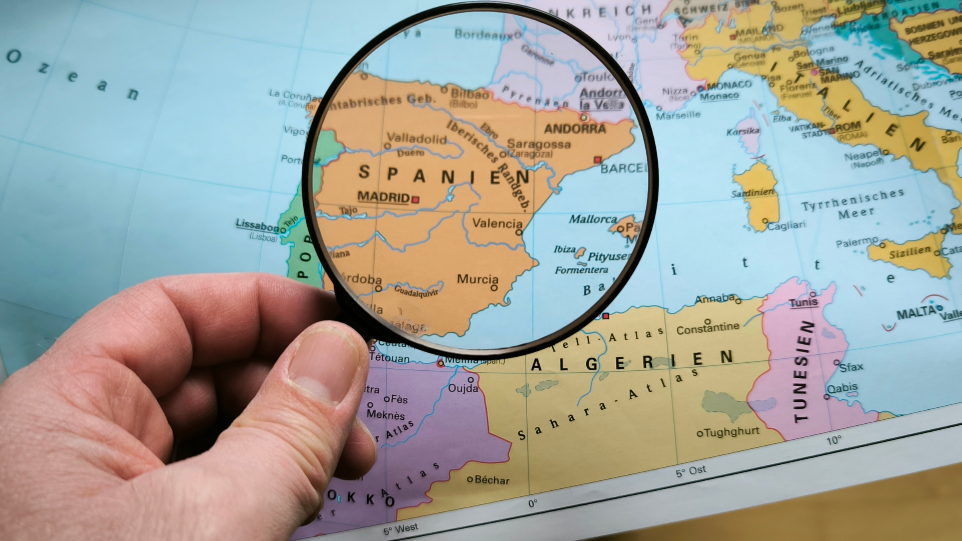 Dłoń trzyma lupę nad mapą.